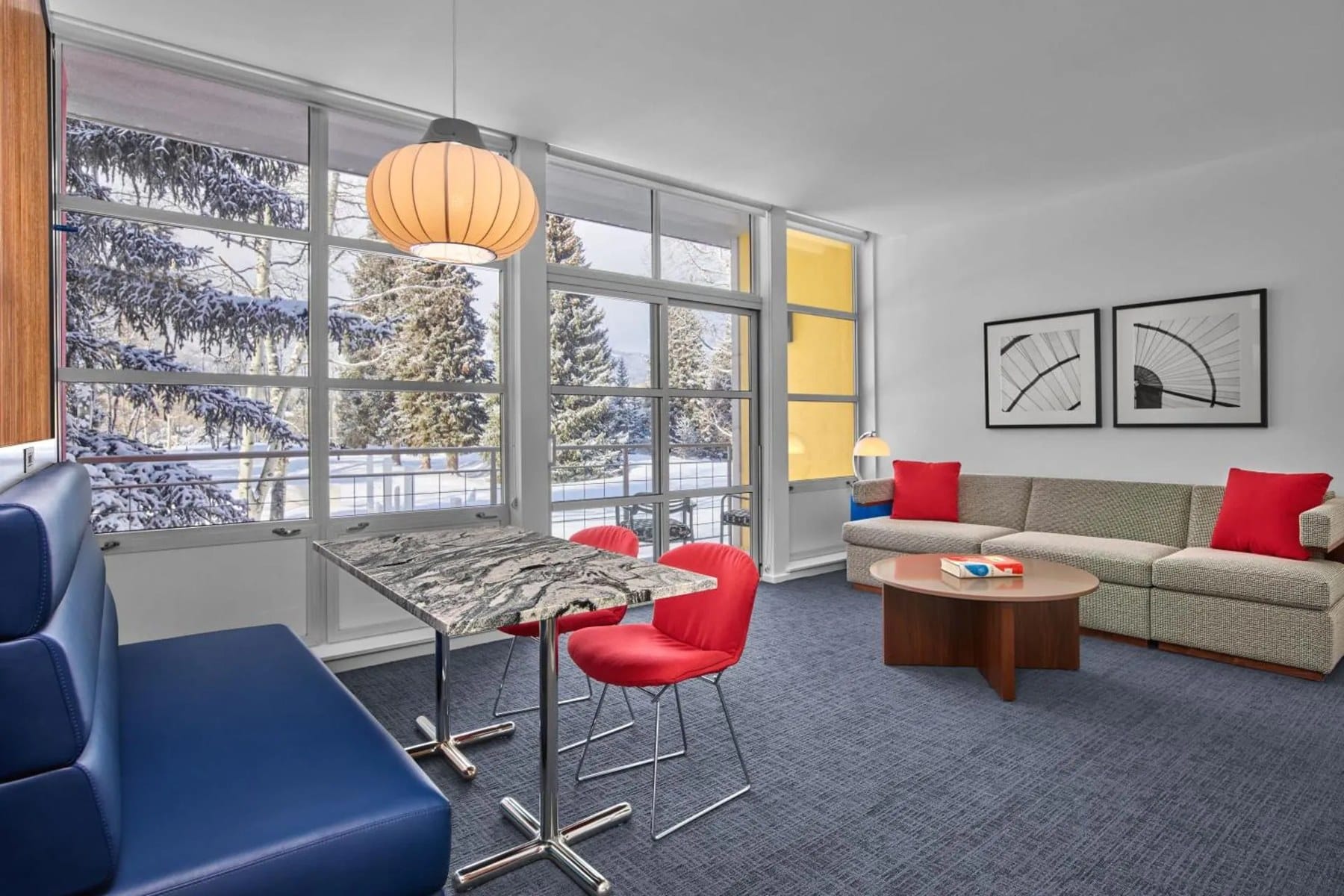 A suite at Aspen Meadows with red chairs, a sofa and a wall of windows onto snowy trees