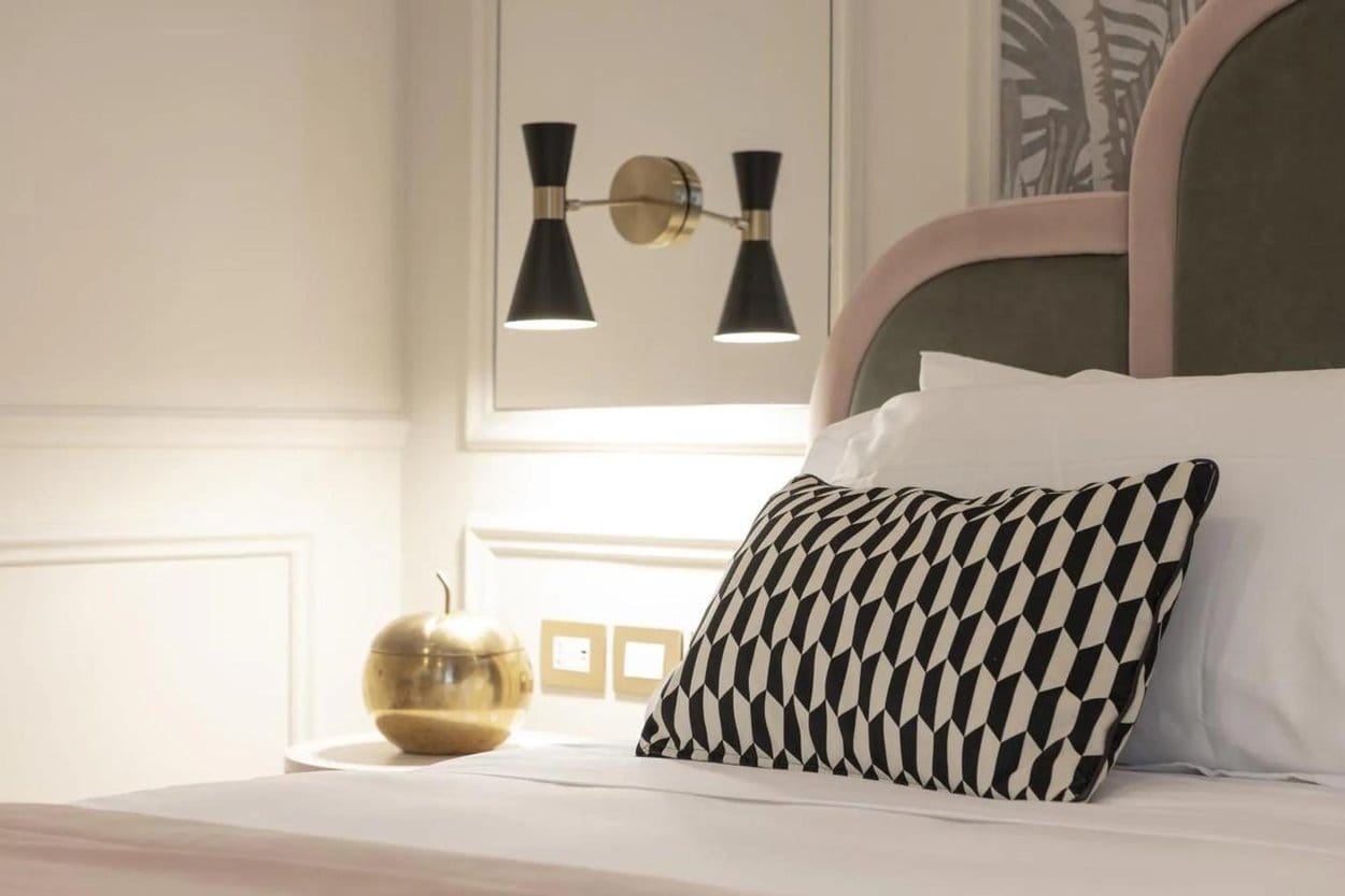 A bedroom at La Gemma, Florence, with a pink and grey velvet headboard, black and white cushion and brass lamps