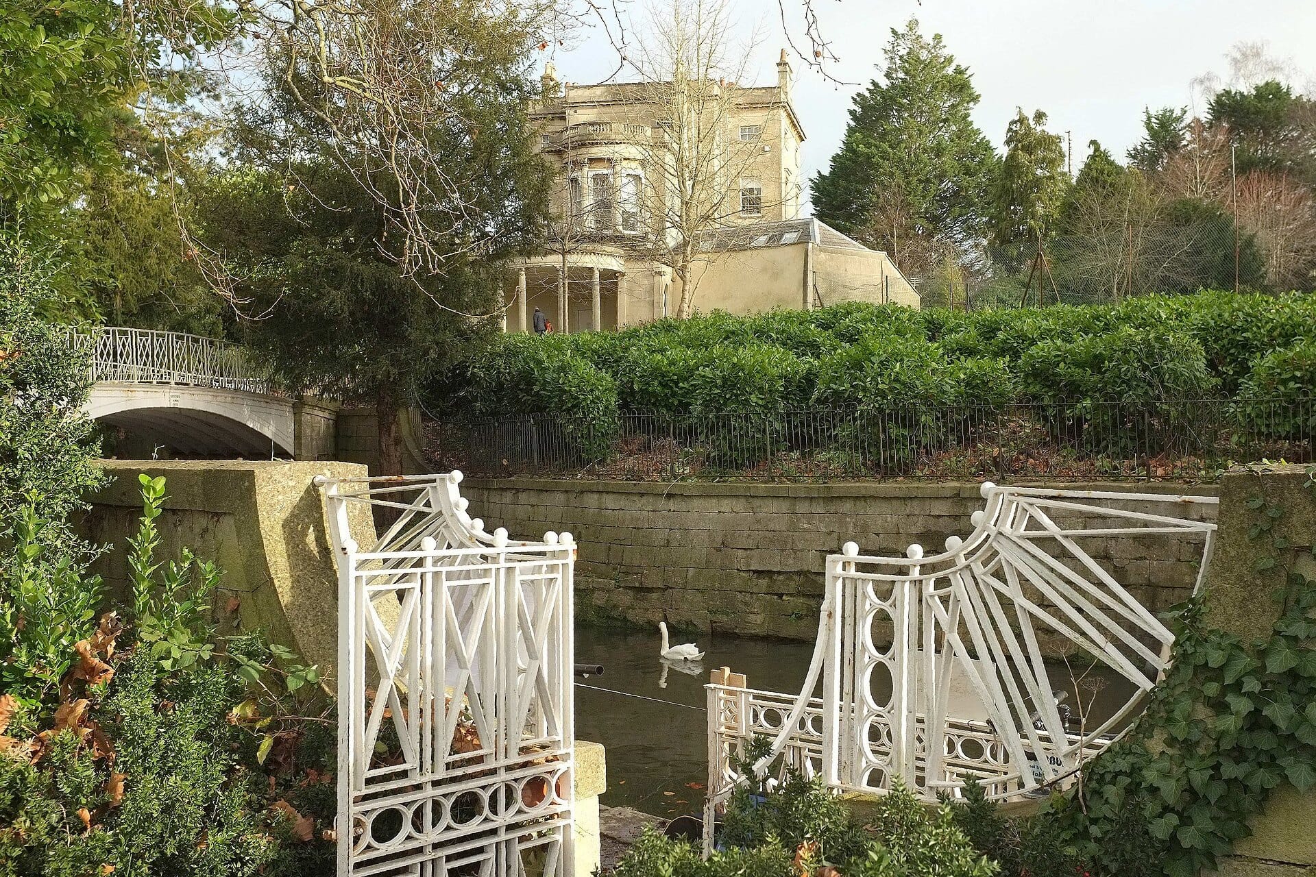 A white Chinoiserie footbridge over the Kennet and Avon Canal in Sydney Gardens, with a swan on the water