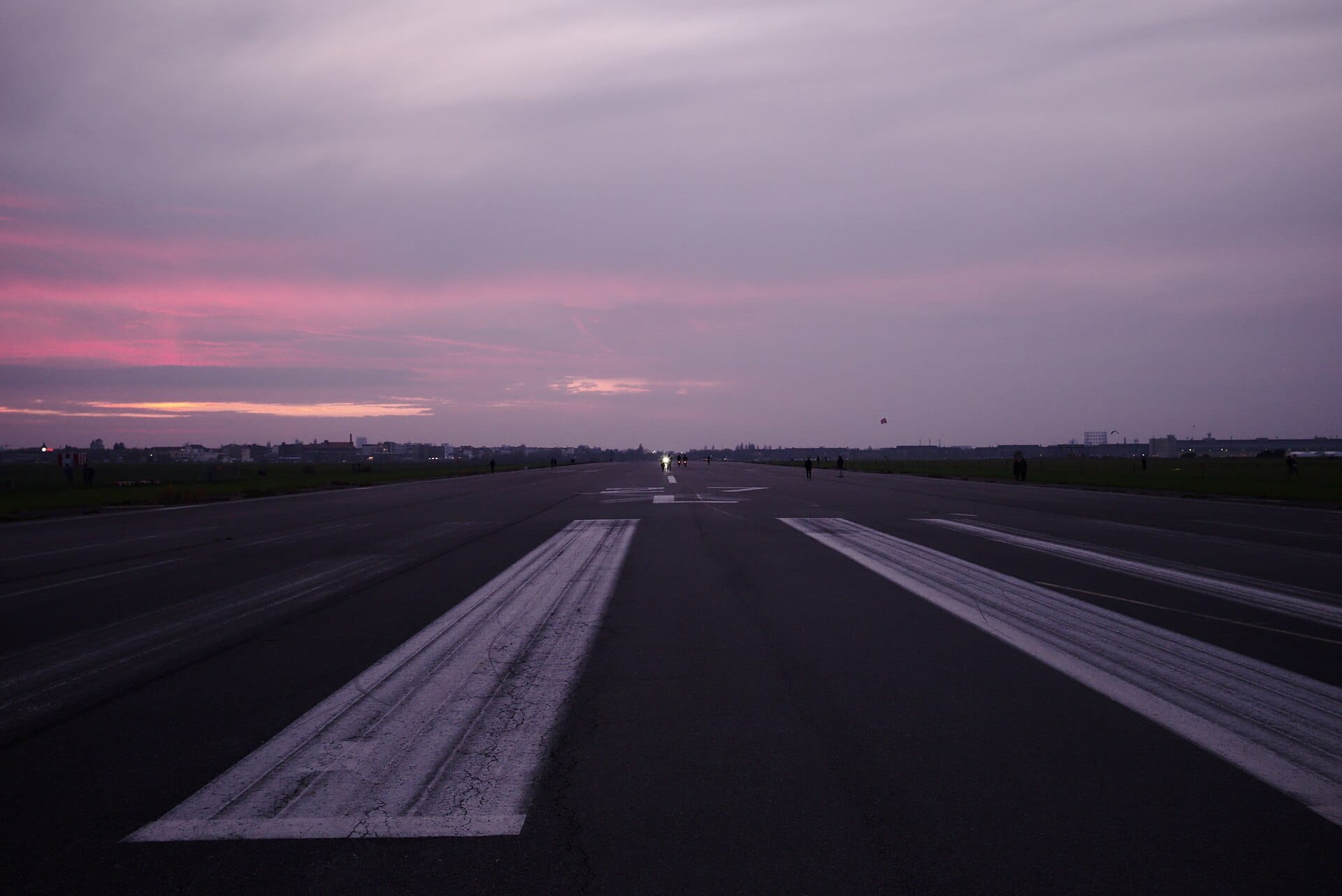 The old runway at Tempelhofer Feld at dusk, with a few people walking far off under a pink sky