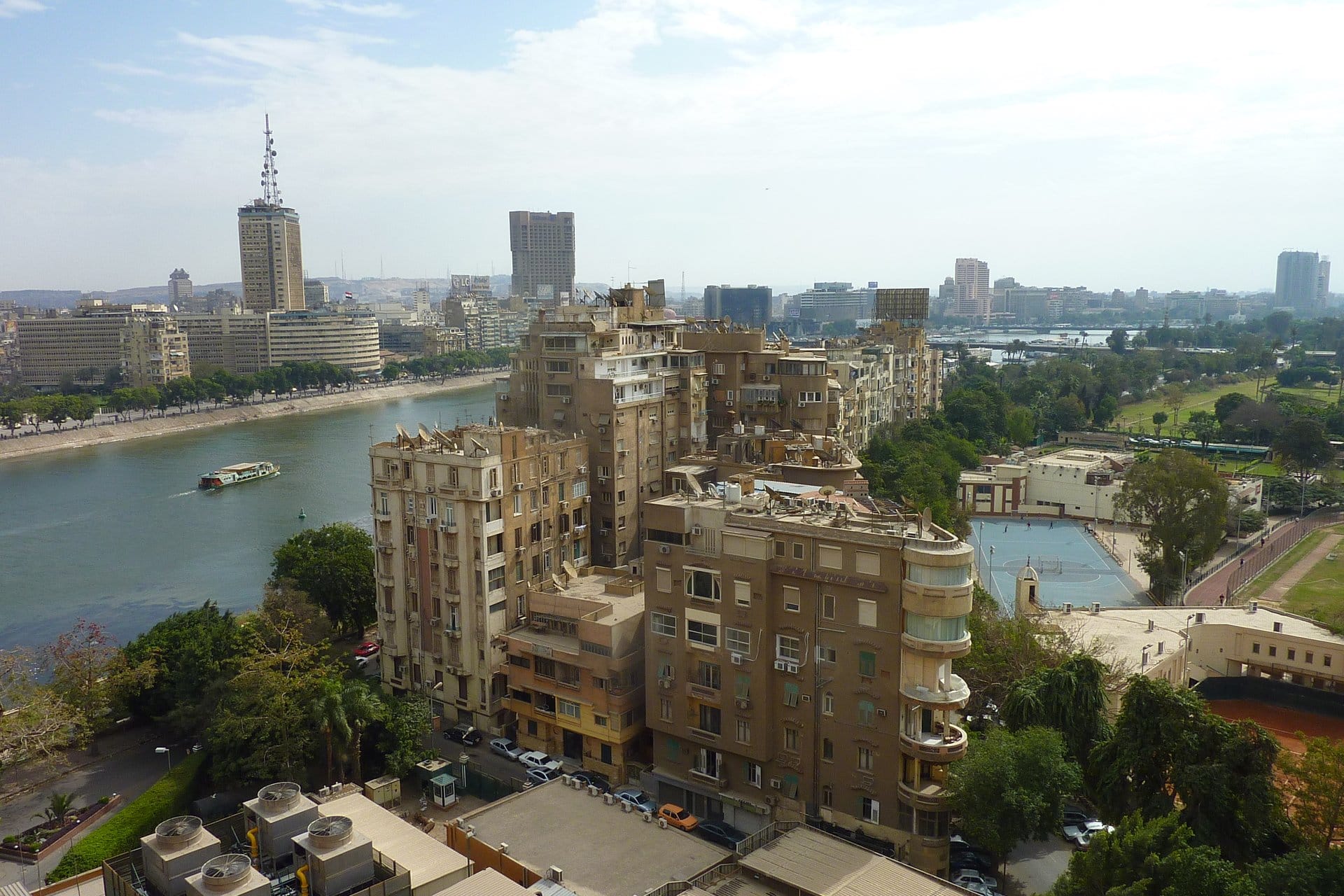 Apartment blocks and gardens on the island of Zamalek beside the Nile, with a river boat and the Cairo skyline beyond