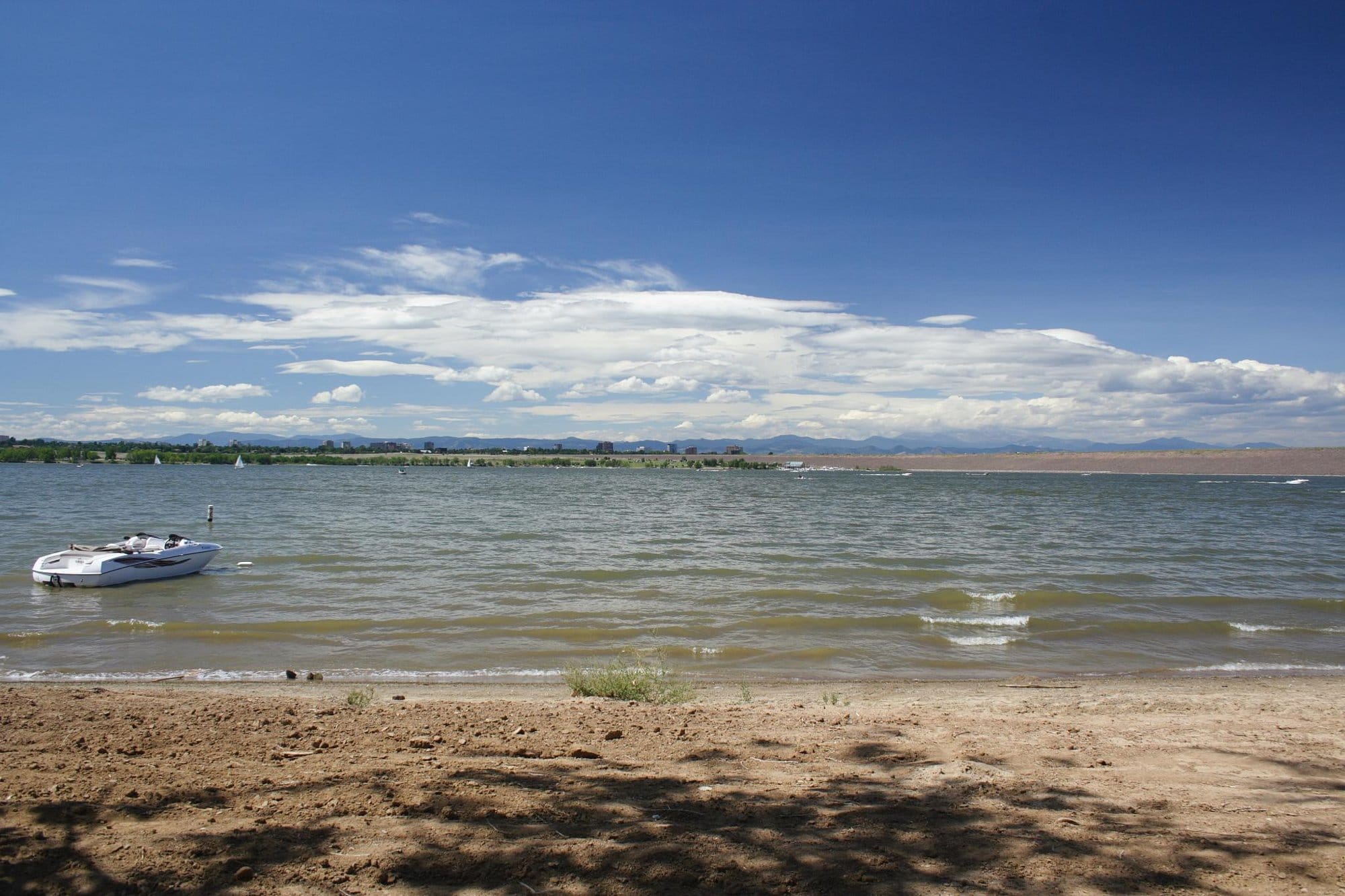 The shore of the lake at Cherry Creek State Park with the Denver skyline and mountains beyond
