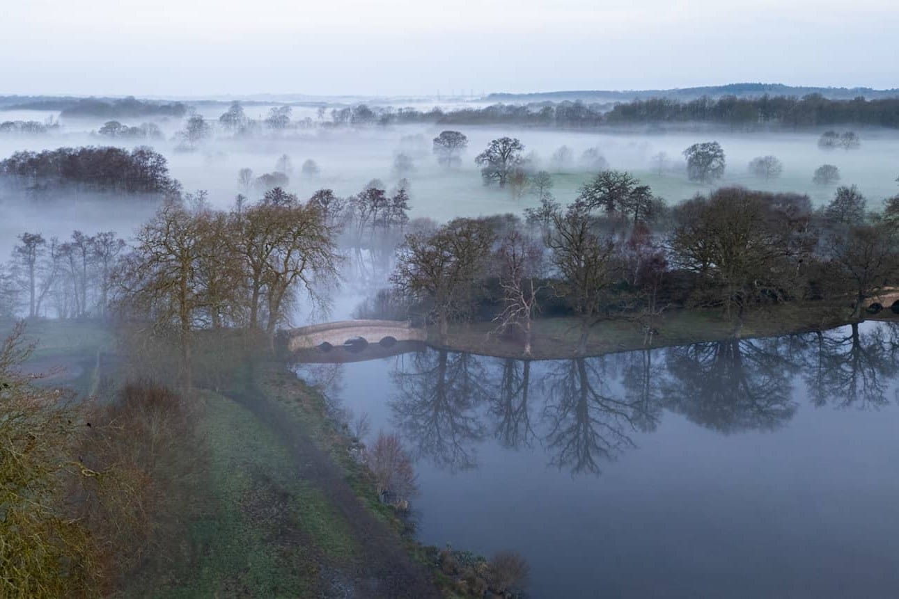 Water, old trees and parkland on the Four Seasons Hotel Hampshire estate under morning mist