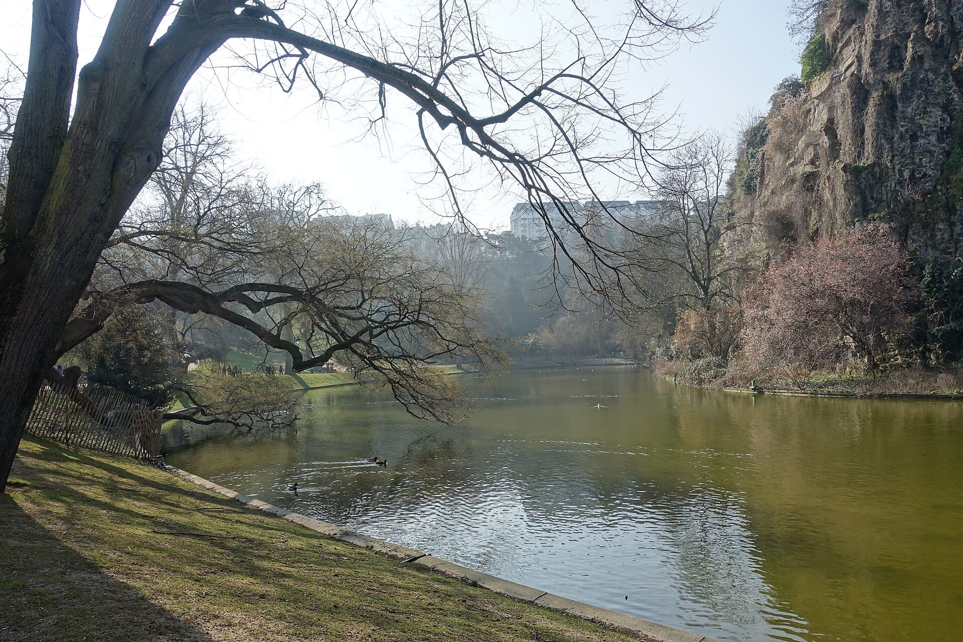 The lake and rocky cliff of the Parc des Buttes-Chaumont framed by bare branches