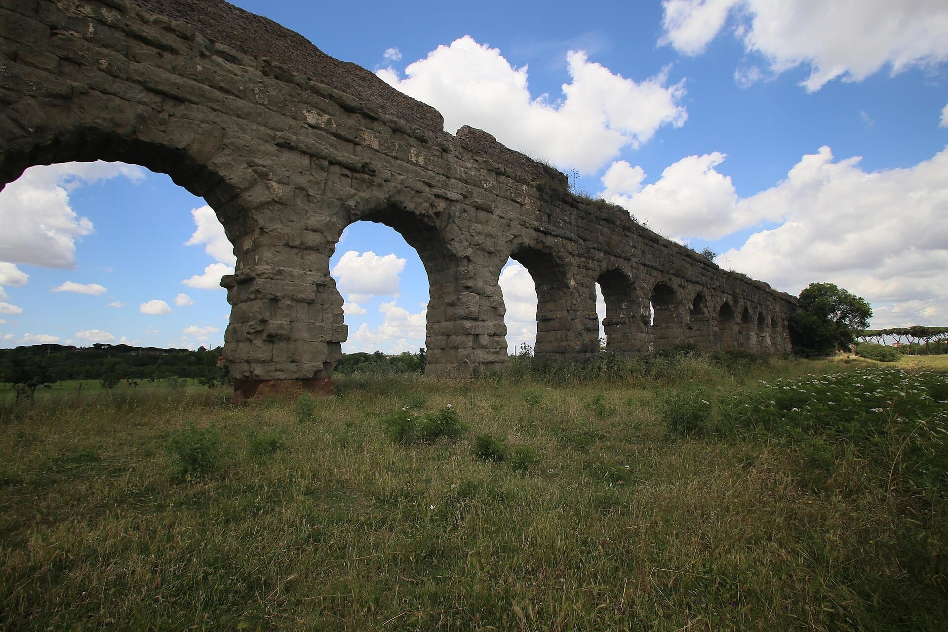 The tall stone arches of a Roman aqueduct crossing open grassland in the Parco degli Acquedotti