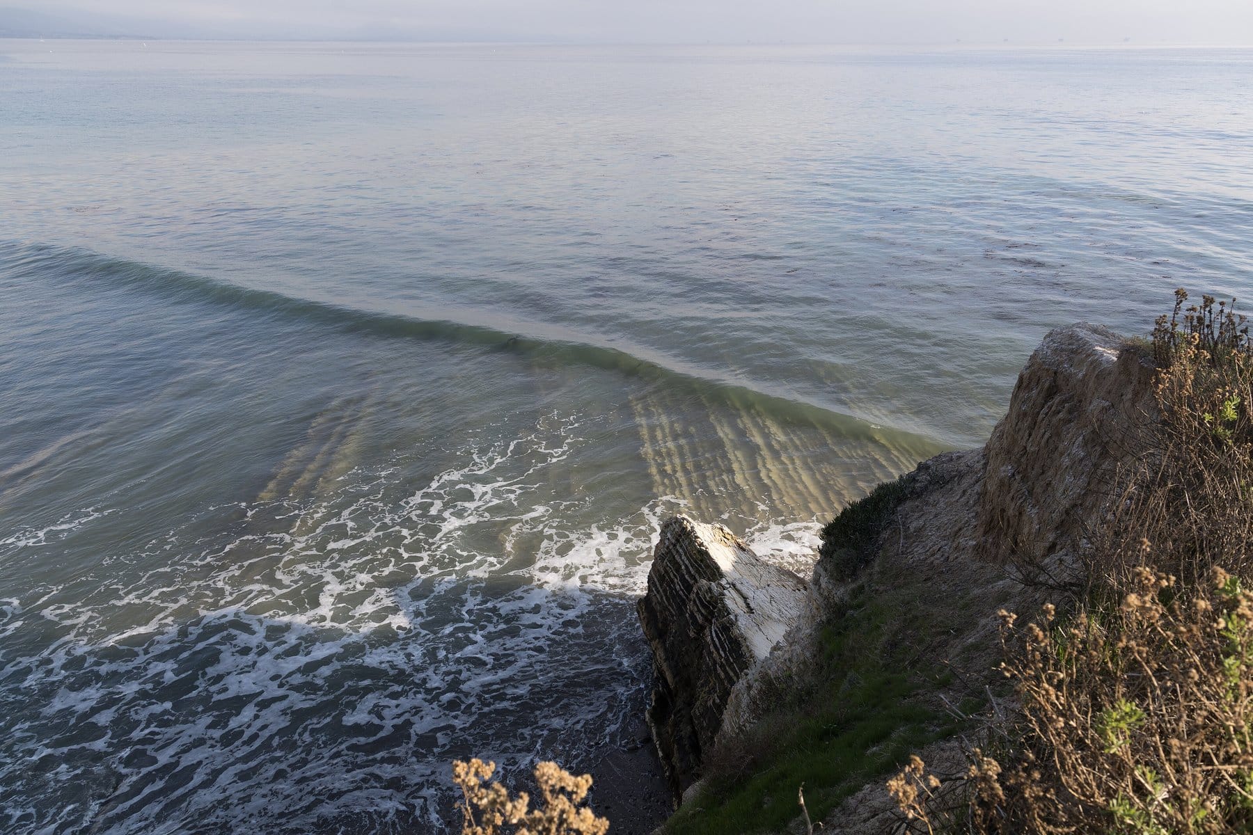 A long wave rolling in past a rocky point on a calm Pacific morning at Santa Barbara Point