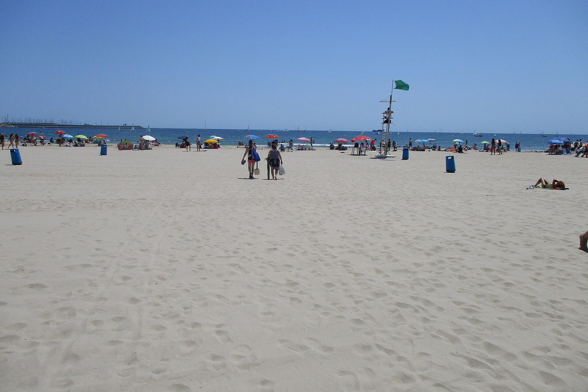 Wide pale sand at Pinedo beach south of Valencia, with walkers heading to the sea and the port breakwater on the horizon