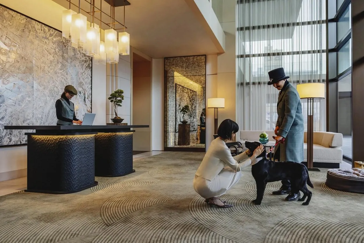 A guest greets a black Labrador in the lobby of Fairmont Tokyo while its owner in a top hat holds the lead