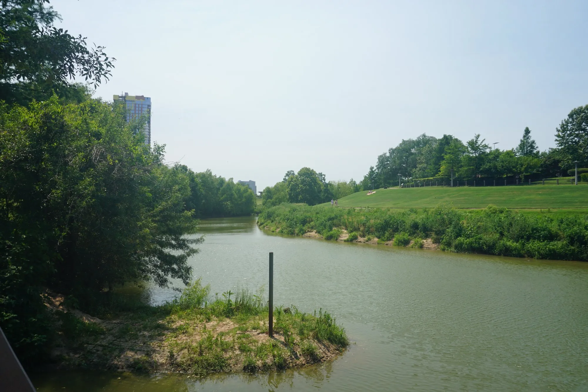Buffalo Bayou winding between green banks and a sloping lawn in Buffalo Bayou Park, Houston