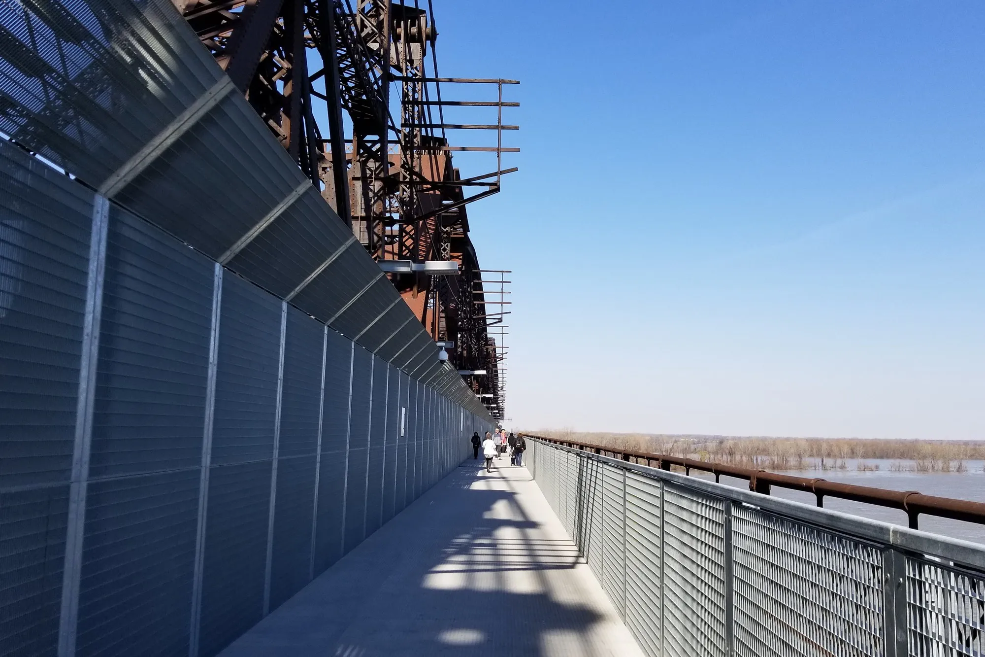 Walkers on the Big River Crossing path beside the steel girders of the old railway bridge, with the Mississippi and its floodplain to the right