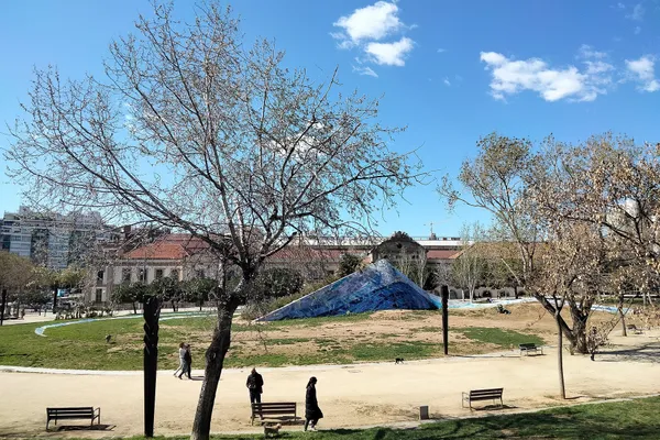 People and dogs on a path through the Parc de l'Estació del Nord, Barcelona, with the blue ceramic sculpture Cel Caigut behind