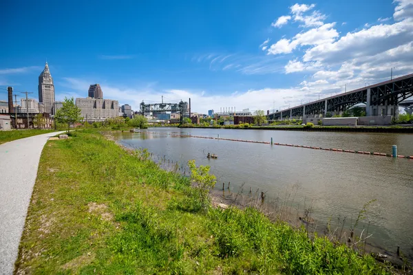 A paved towpath trail running beside the Cuyahoga River, with downtown Cleveland's towers and a lift bridge beyond
