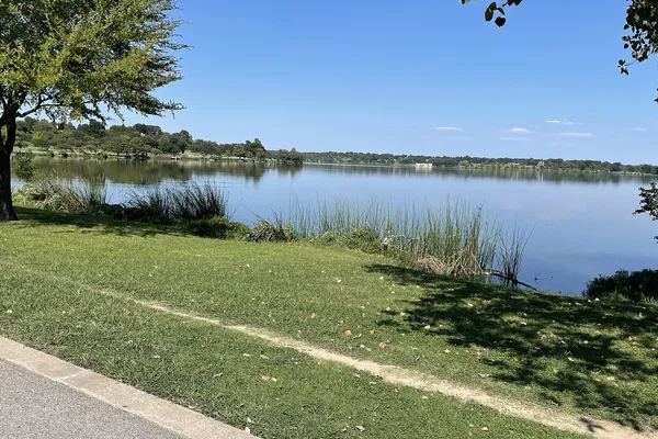 A grassy shoreline path beside White Rock Lake in Dallas under a clear blue sky