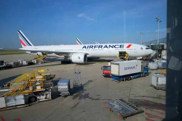 An Air France Boeing 777 at a gate at Paris Charles de Gaulle with ground crew and baggage carts