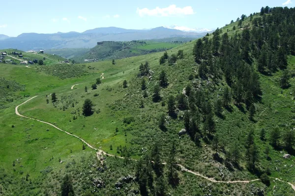 A dirt trail winding across green foothill slopes at Horsetooth Mountain Open Space with mountains on the horizon