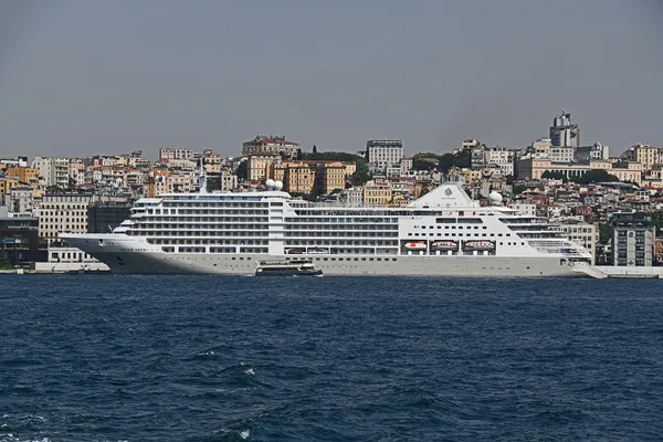 A white cruise ship moored at Galataport on the Karaköy shore of the Bosphorus, with the hillside houses of Beyoğlu and Cihangir behind