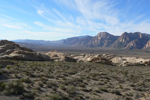 Desert scrub and sandstone outcrops in Red Rock Canyon with walkers on a trail and the escarpment beyond