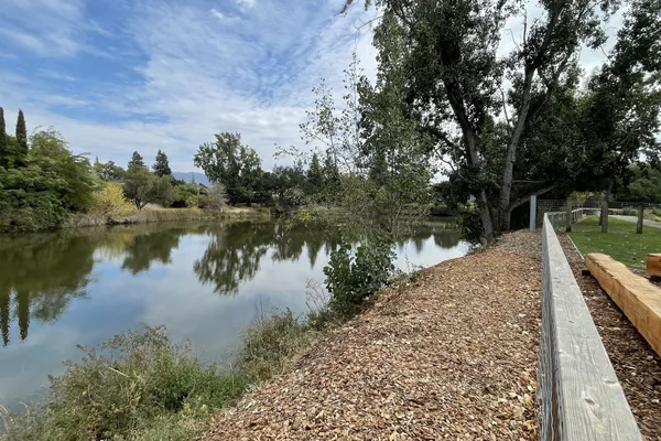 The Napa River lined with trees under a blue sky, with a woodchip path and a wooden rail running along the bank beside Napa Yard, Napa