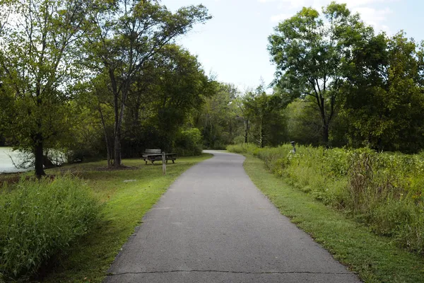 A paved greenway path curving between trees and meadow beside a pond in Shelby Bottoms, Nashville