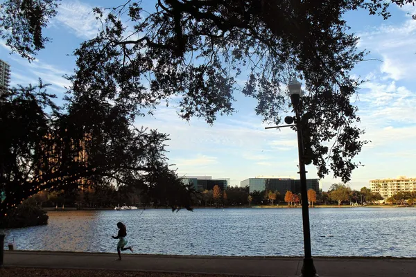 A lakeside path under live oaks at Lake Eola Park, with the water and downtown Orlando beyond