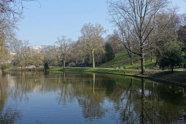 Walkers on a path beside the lake in the Parc des Buttes-Chaumont, Paris, on a clear winter day