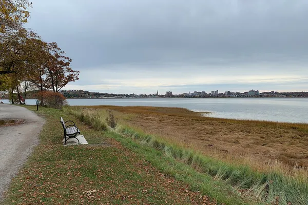 A stone dust path and a bench beside autumn trees and salt marsh on Back Cove, with the Portland skyline across the water