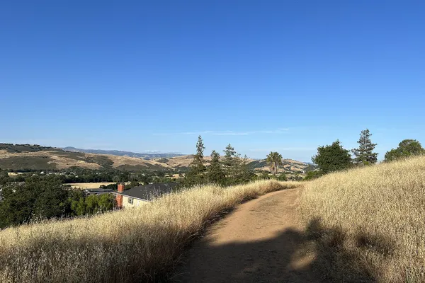 A dirt trail through golden grass on a ridge in Almaden Quicksilver County Park, with hills beyond