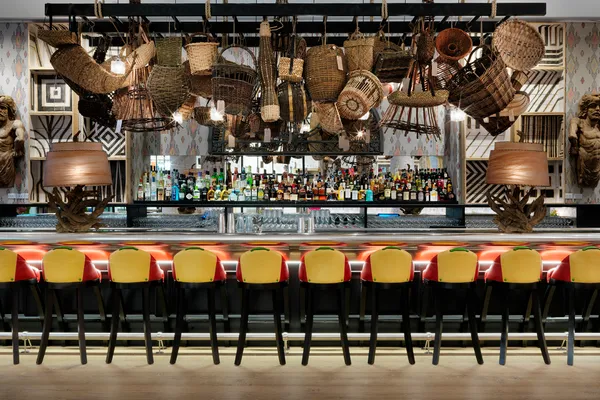 The Whitby Bar, with woven baskets hung above a long pewter topped bar and yellow bar stools
